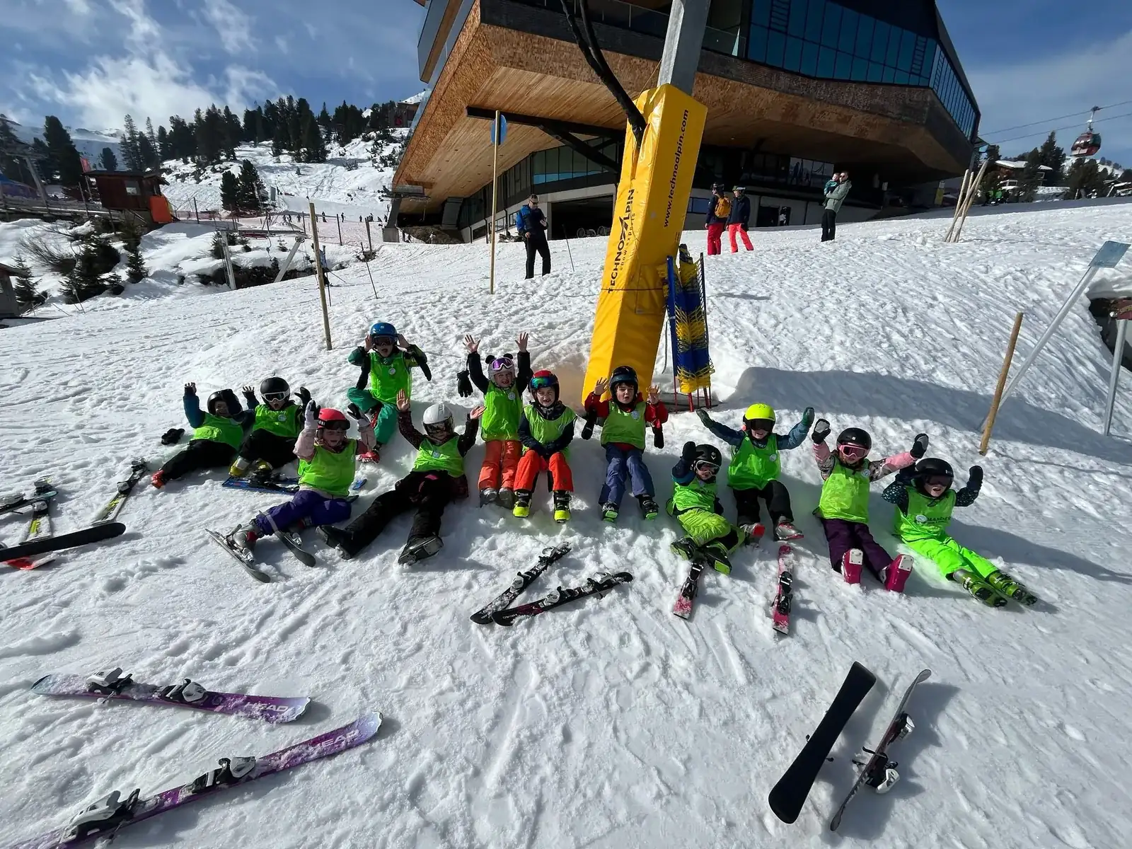 Een skigroepje ligt en zit in de sneeuw bij het bergstation