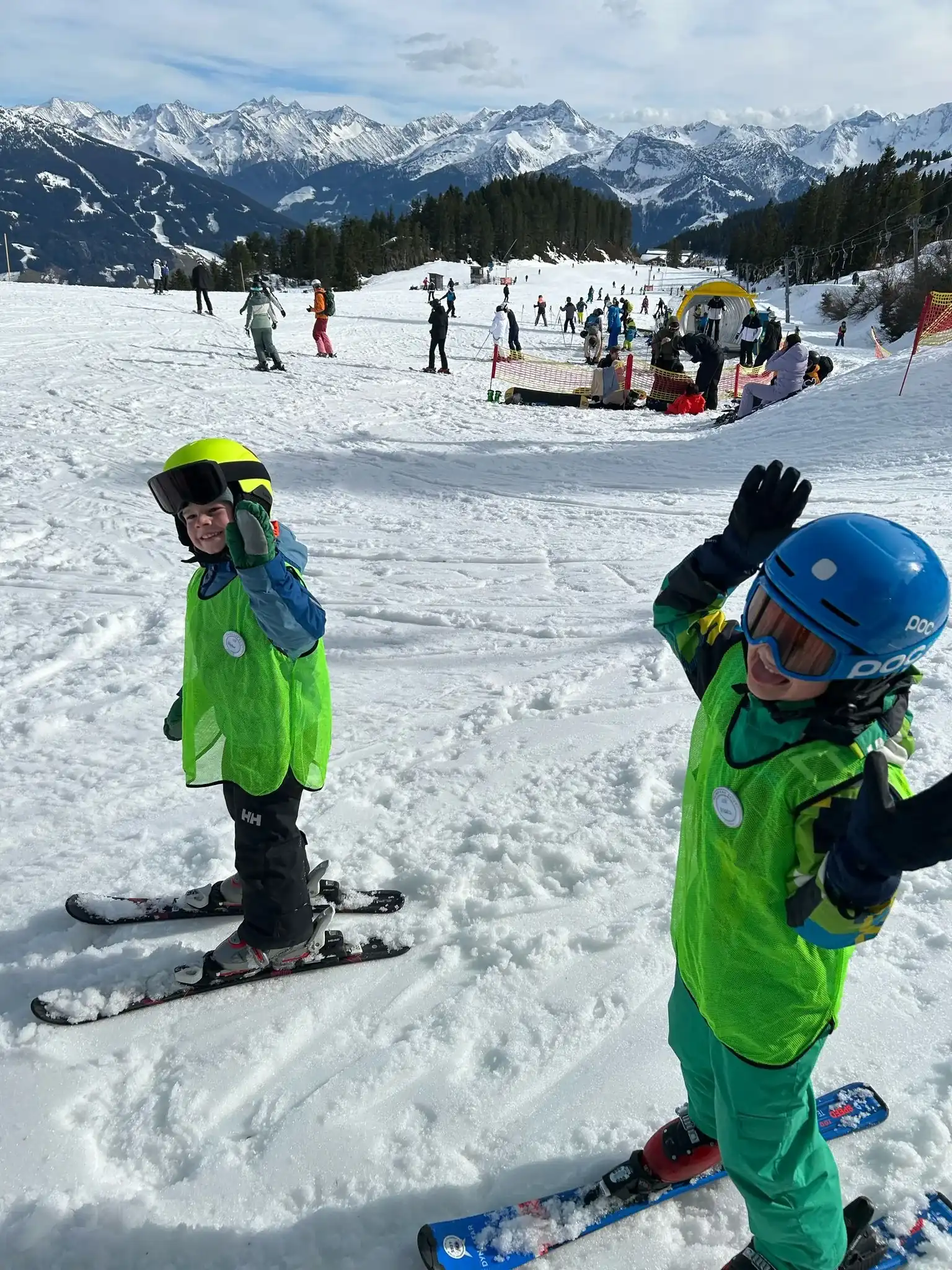 Twee kinderen in groene hesjes zwaaien op de piste